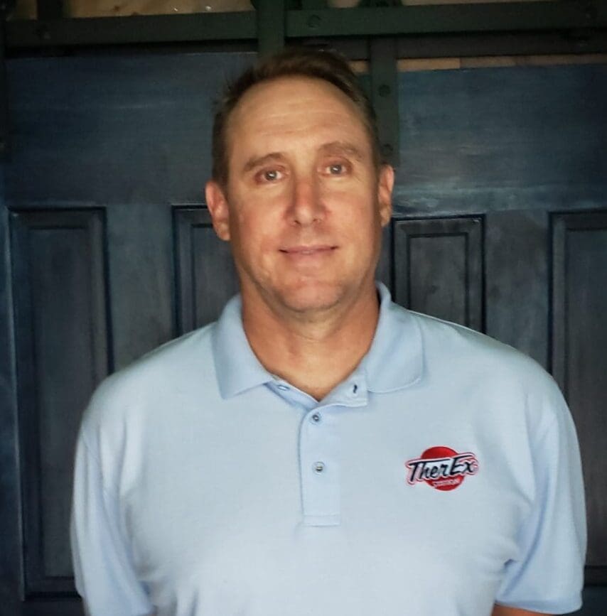 A man in a blue shirt standing next to a wooden door.