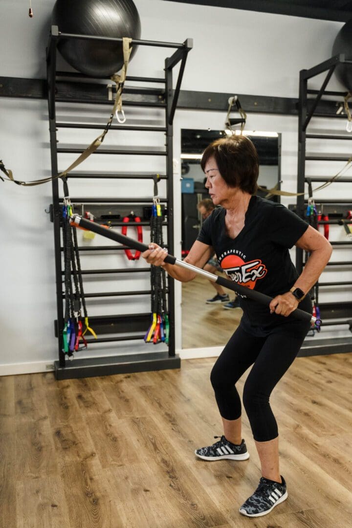 A lady in the gym holding a rod and working out
